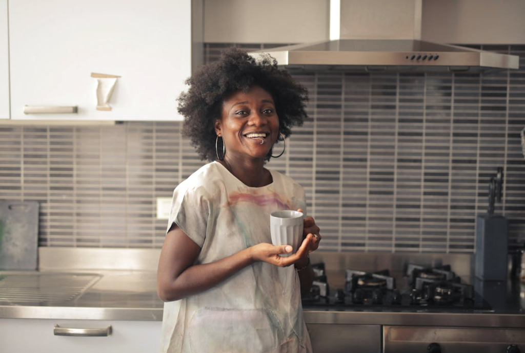 Woman smiling in a modern kitchen holding a mug, representing personal growth, healthy routines, and daily habits for mental and physical well-being.